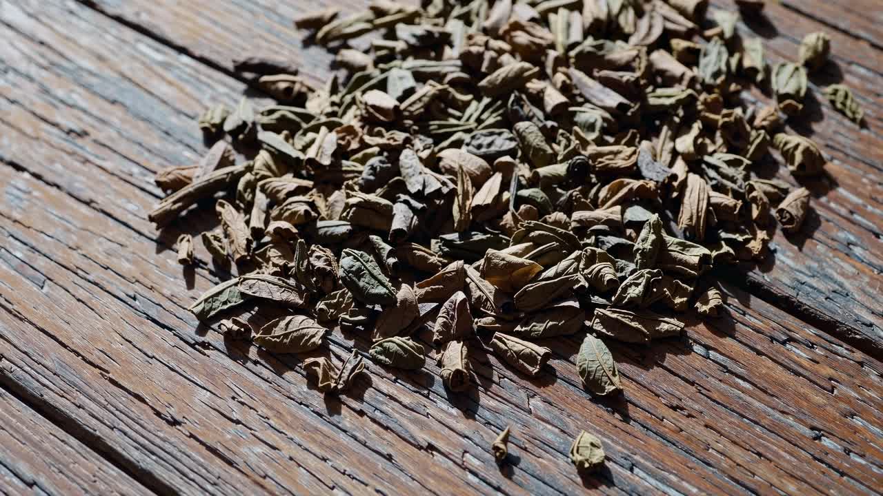 Close-up video of dried herbs scattered on rustic wooden surface, captured from a low angle