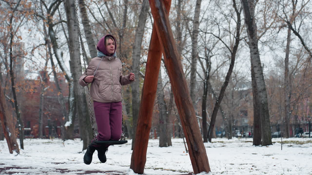 겨울을 위해 옷을 입은 여자가 눈 인 놀이터에서 야외에서 스을 즐기고, 벌거벗은 나무로 둘러싸여 조용하고 평화로운 겨울의 진동을 포착합니다.