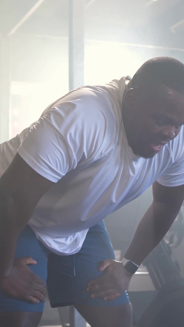 Vertical video: Gripping battle ropes, fit man swinging rapid waves for cardio in gym, white tee