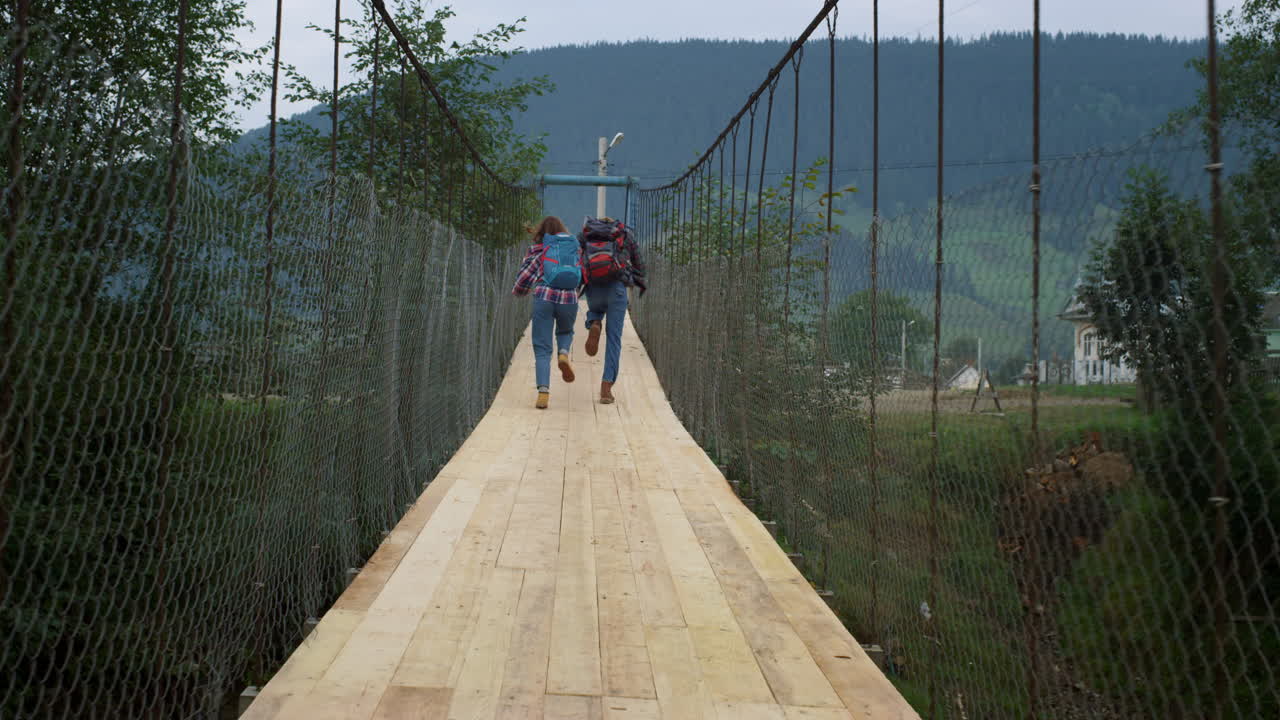 Friends run racing outdoors on mountains bridge. Tourists wear backpacks on hike