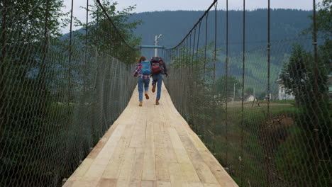 friends run racing outdoors on mountains bridge. tourists wear backpacks on hike