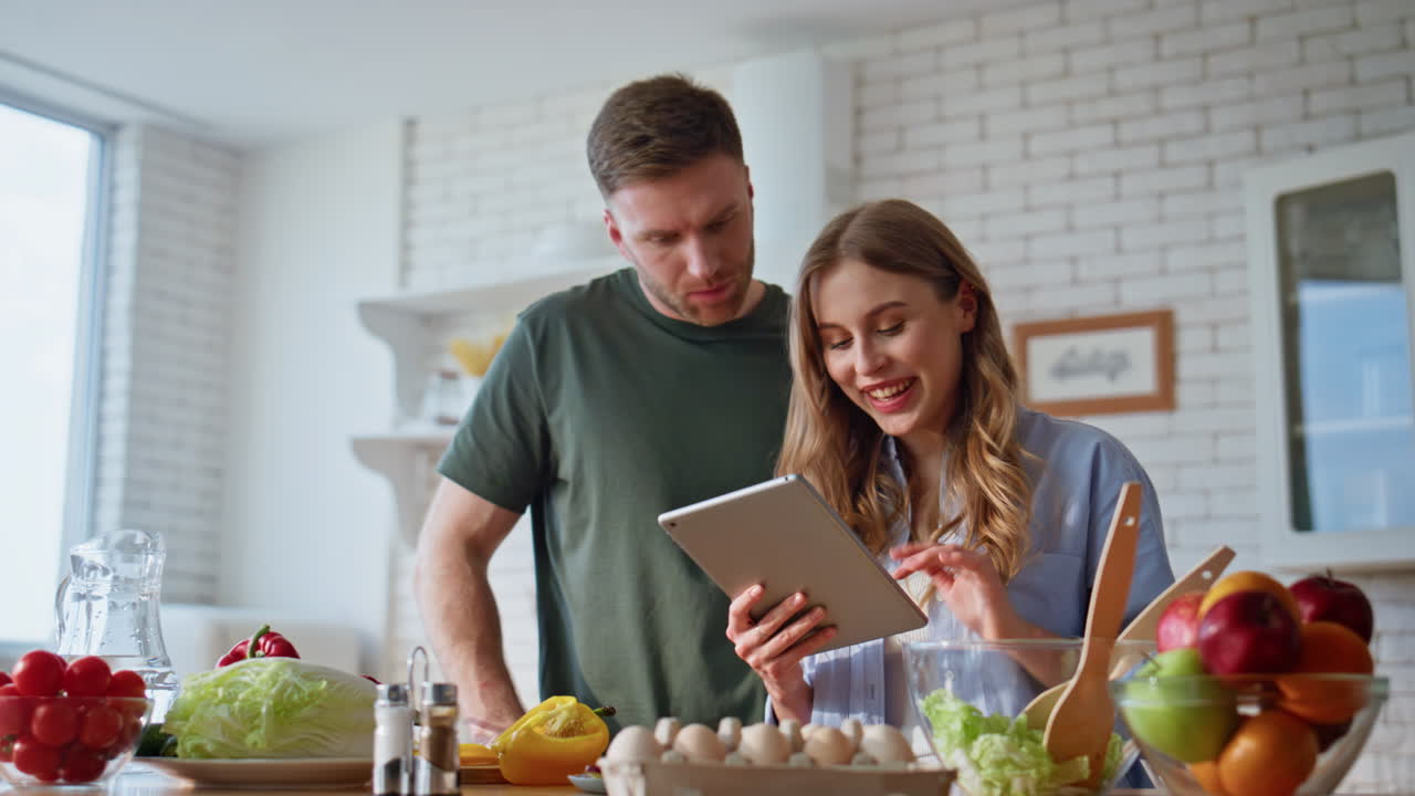 Cooking pair using tablet in kitchen at morning closeup. Couple looking recipe