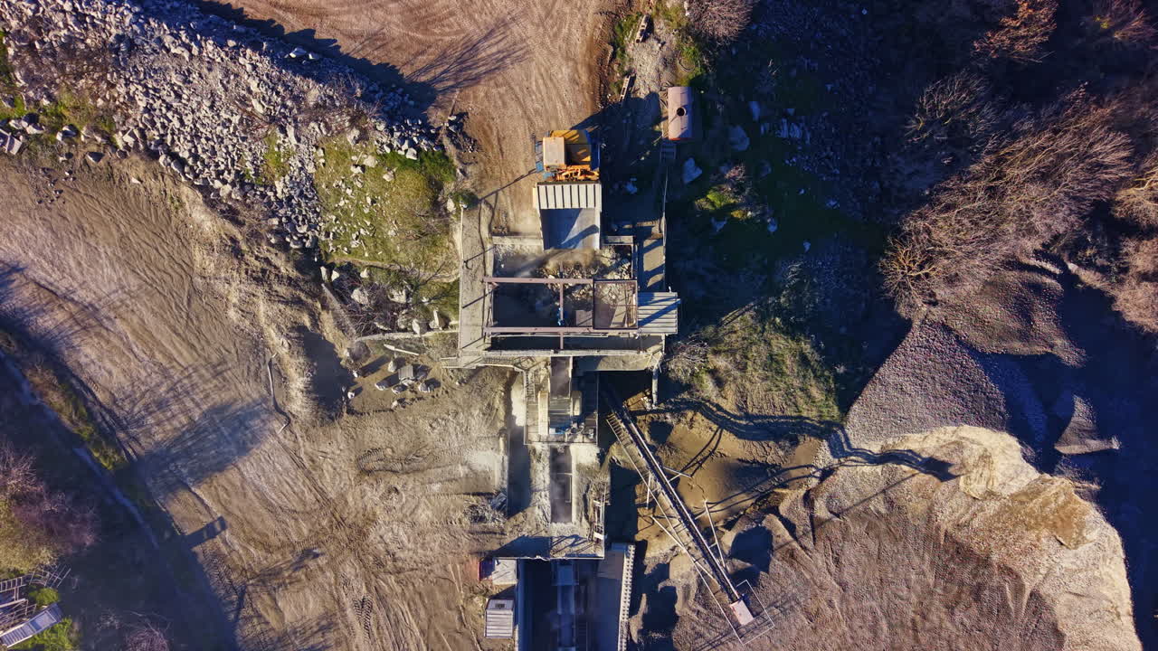 Industrial site captured from above, showcasing machinery and gravel processing in a rugged landscape on a sunny afternoon