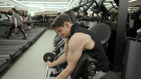 hombre haciendo rizos de bíceps con barra en el banco de scott en el gimnasio moderno