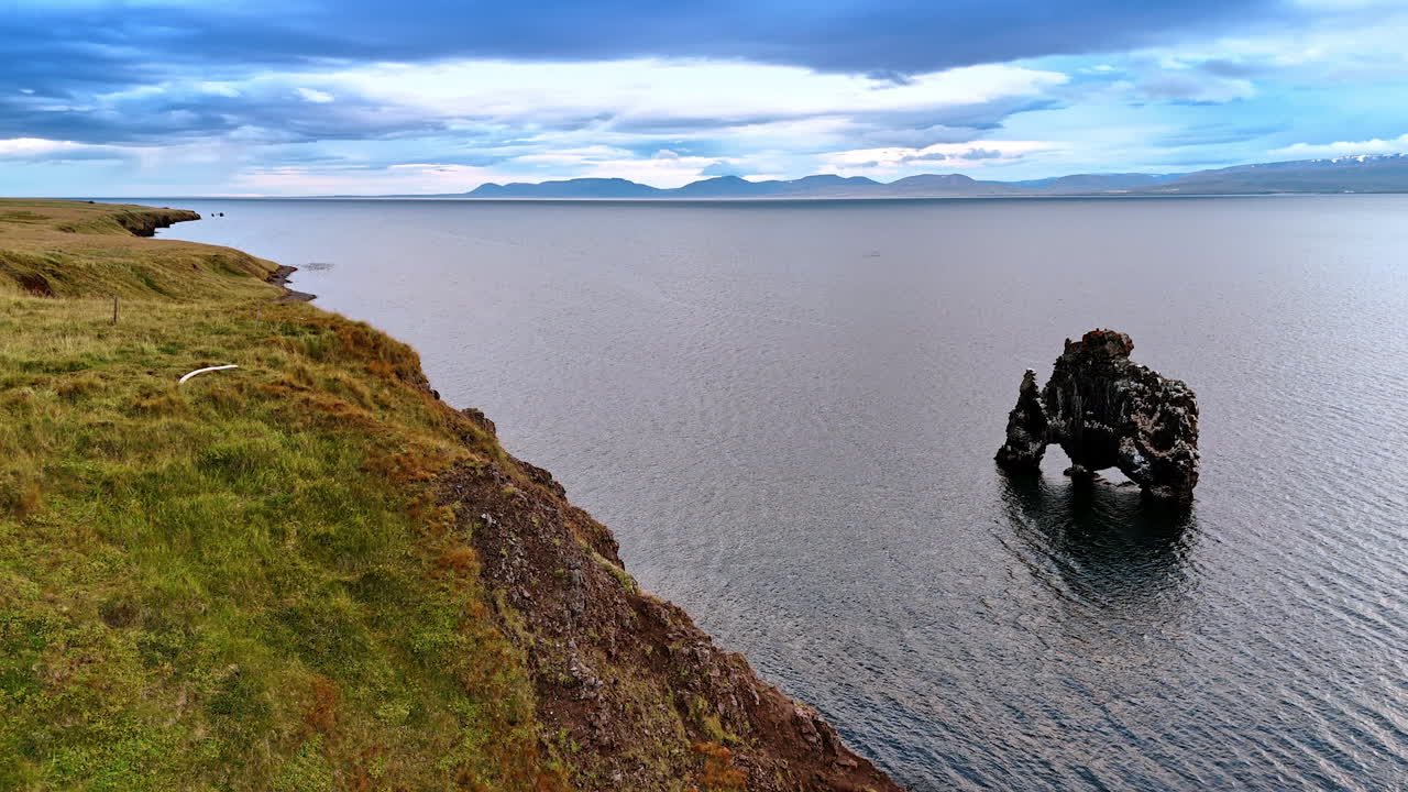 Unusually-shaped crooked black rock peeping out of water. Coast of Iceland on gloomy daytime. Top view.