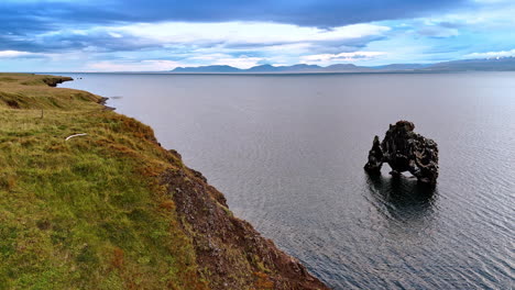 unusually-shaped crooked black rock peeping out of water. coast of iceland on gloomy daytime. top view.