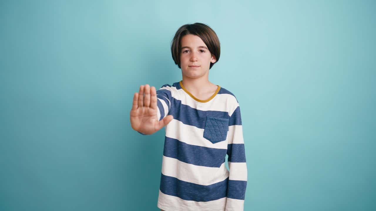 Giovane ragazzo che fa un gesto di stop con la mano su sfondo blu.
