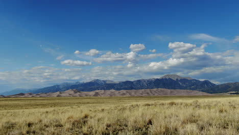 aerial cinematic drone late summer opening view entrance of the great sand dunes national park colorado rocky mountain 14er peaks crisp golden yellow tall grass blue sky slide to the left movement