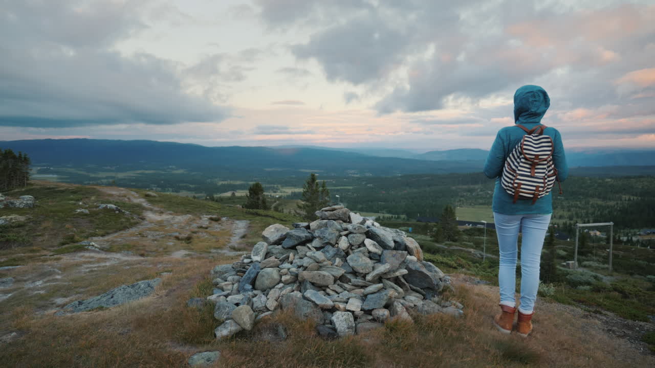 una mujer está de pie en un montón de piedras en una montaña en el fondo de un cielo dramático una vista trasera