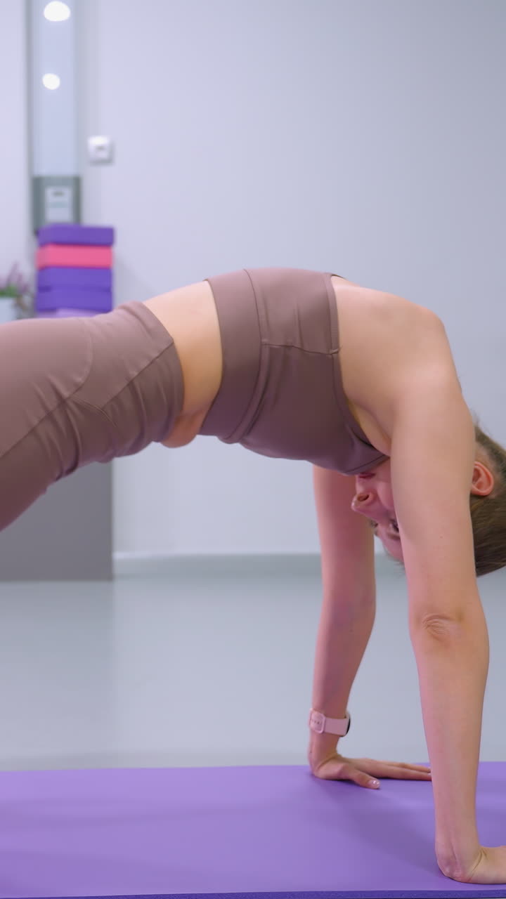 vista lateral de una mujer realizando un estiramiento profundo en una alfombra púrpura en un gimnasio bien iluminado, centrarse en la alineación del cuerpo, la fuerza central y la flexibilidad