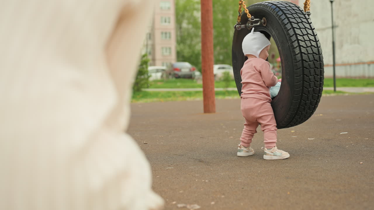 Young Child Playing In Park, Toddler Stabilizing Himself At Playground, Little One Balancing Himself Near Tire Swing Outdoors, Small Child Dressed In Pink Carefully Holding Tire Swing For Balance