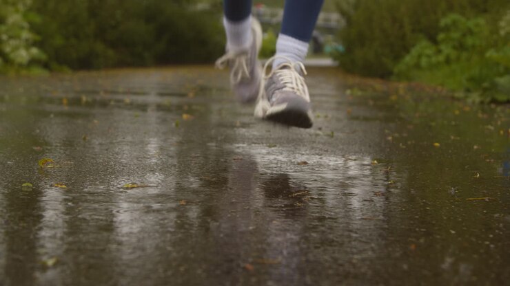 Primer plano desenfocado de mujer haciendo ejercicio para mantenerse en forma, corriendo bajo la lluvia hacia la cámara 1