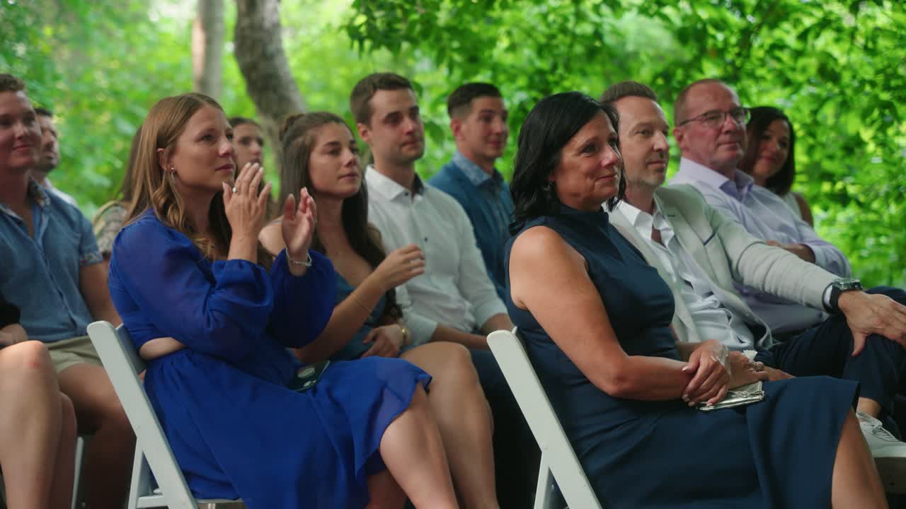 Women sitting on inside aisle of outdoor wedding ceremony, happily crying while looking toward the couple