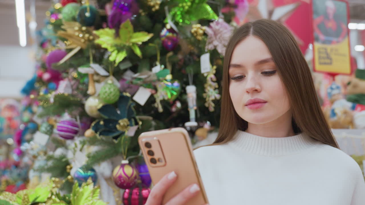 Elegant lady in white sweater takes a picture with her phone in front of a beautifully decorated Christmas tree at a well-lit holiday decor store