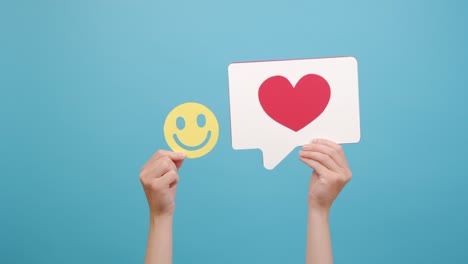 close up of female hands holding reaction icon share repost comment popular click and yellow happy smiley face, good feedback, isolated on blue studio background wall. blogger and online concept