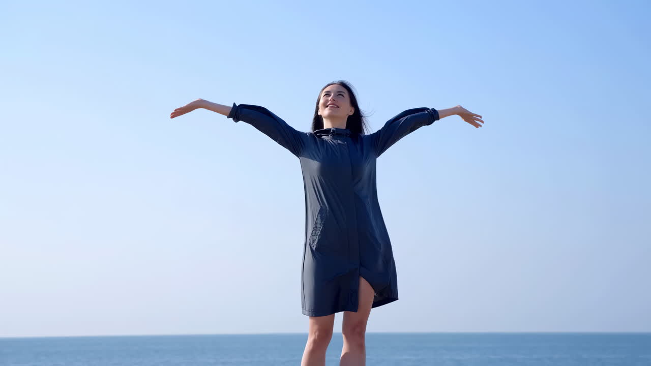 海辺で両腕を広げて立っている若い女性。
