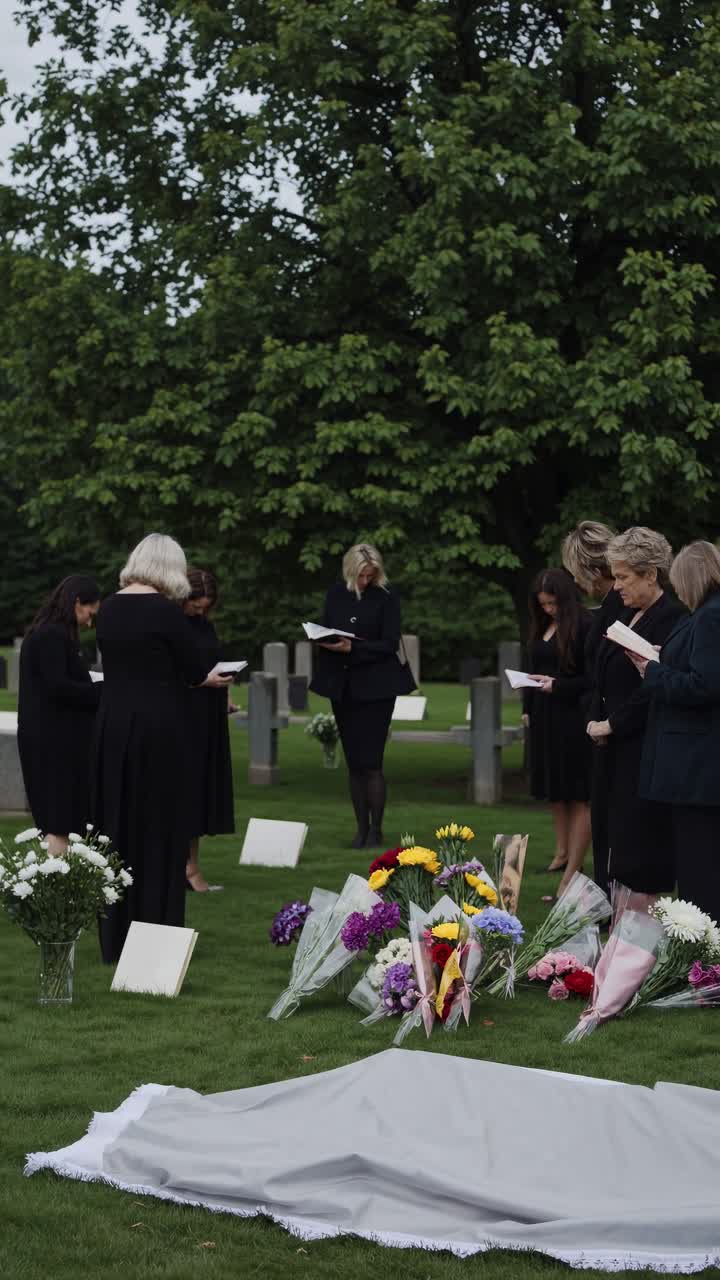 Gruppo di donne in abito nero che leggono a un funerale al cimitero