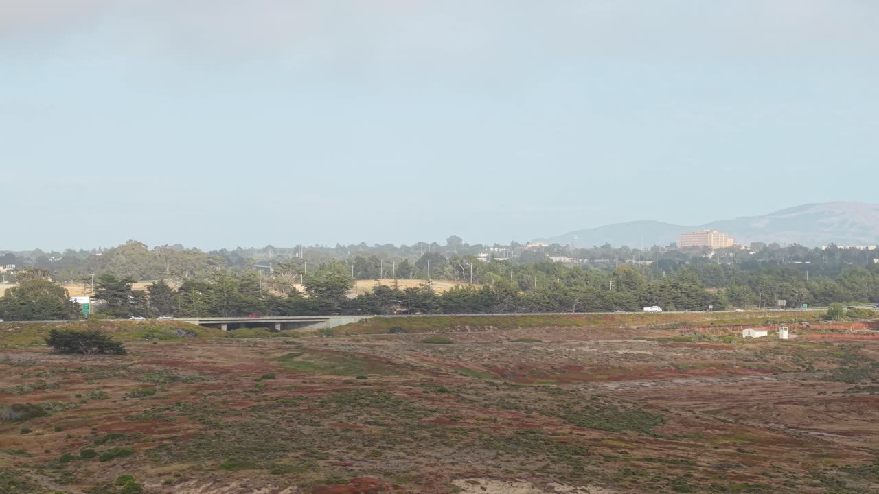 The drone glides over sandy terrain and low brush, revealing Highway 1 as a silver ribbon in the distance.