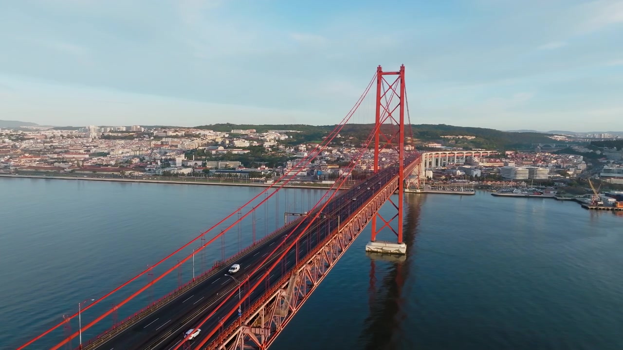 Ripresa panoramica con drone in volo sopra il Ponte 25 de Abril, Lisbona, Portogallo. Giornata di sole, cielo sereno, alba. Fiume Tago sottostante. Filmato aereo cinematografico di infrastrutture