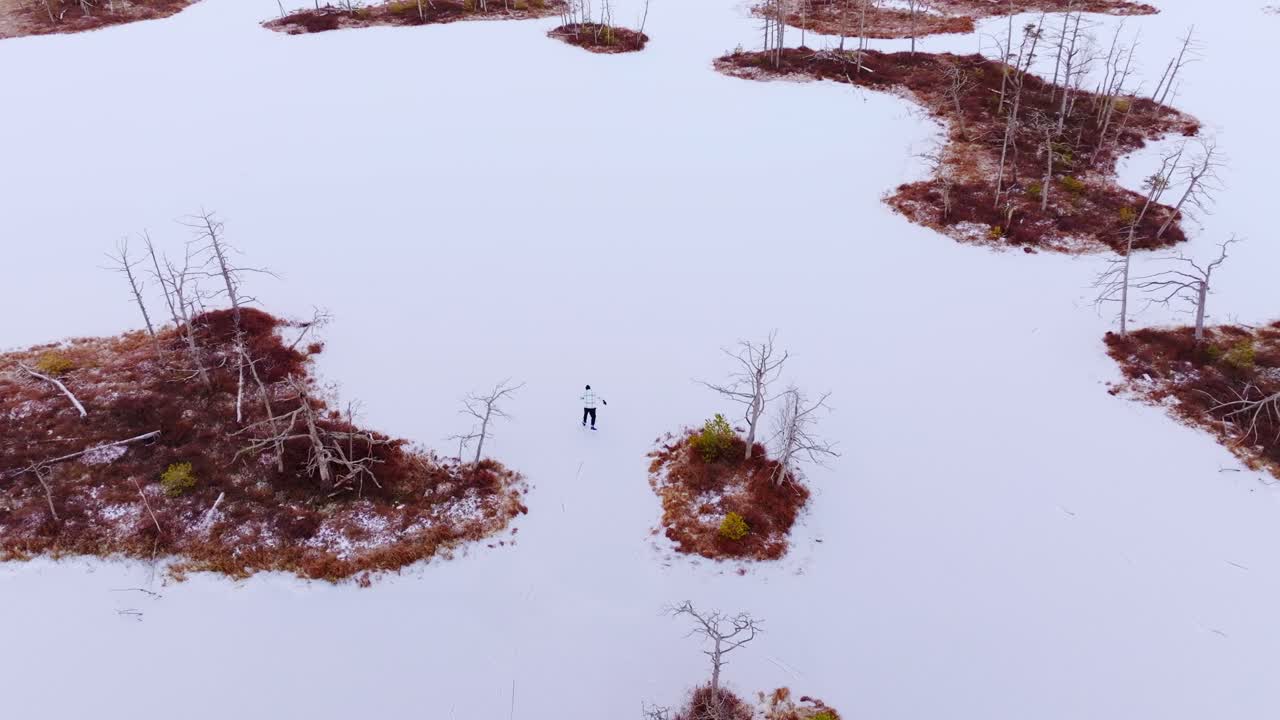 Aerial shot of skater gliding across frozen white lake in quiet Cenu Tīrelis bog