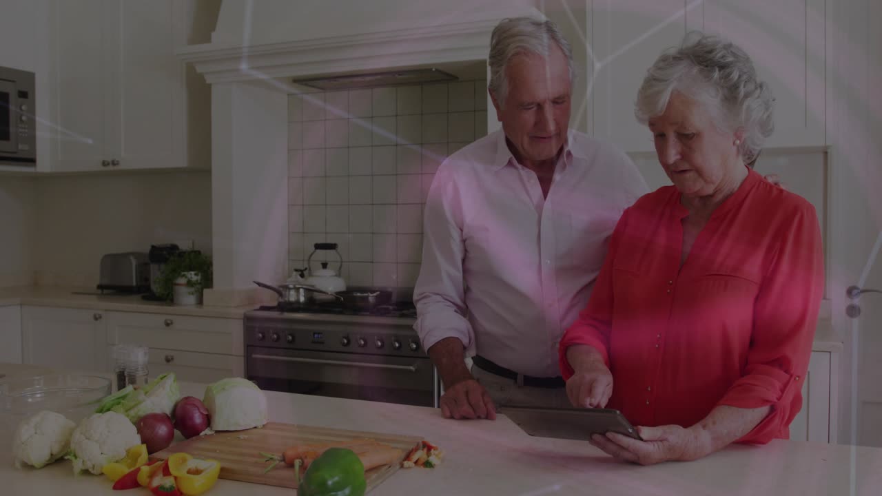 Coppia di anziani che taglia le verdure in cucina toccando il tablet per visualizzare le icone durante un tutorial di cucina