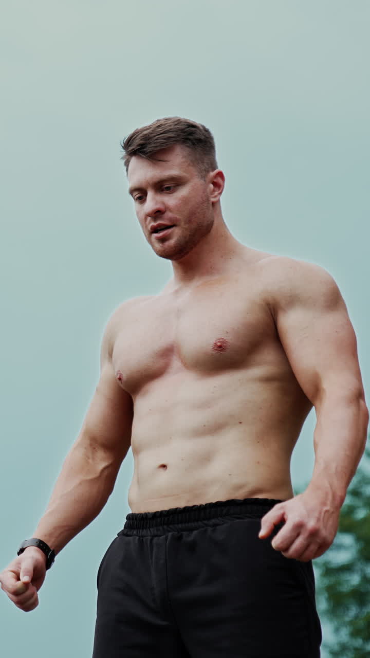 Strong Caucasian man with naked torso stands outdoors. Sportive healthy lifestyle concept. Low angle view. Vertical video