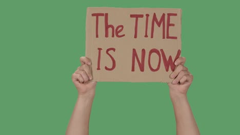 showing cardboard poster with inscription the time is now. human rights demonstration. hands holding a poster a green screen, chroma key. close up. slow motion