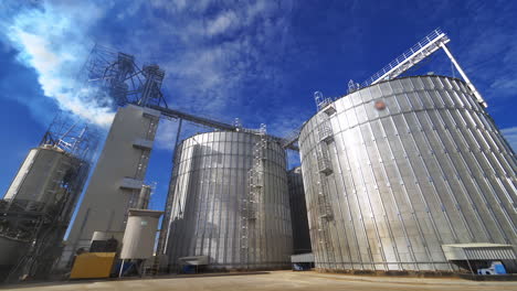 huge granary outdoors. large metal elevators on sky background. white smoke released into the air from industrial silos.