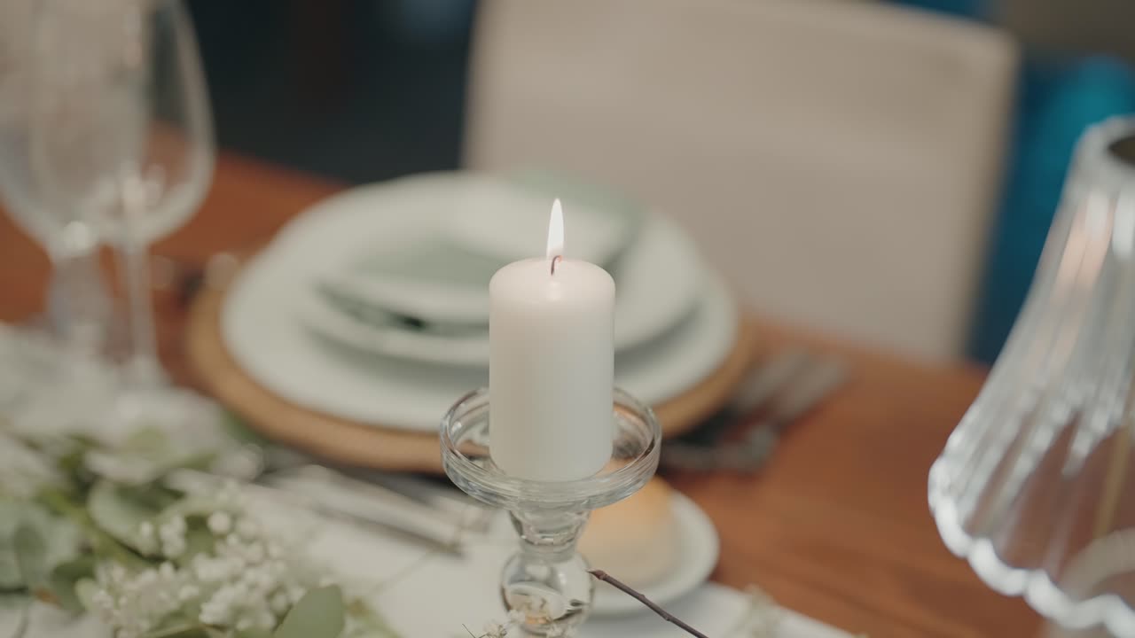 Close up of a white candle burning on a glass holder with decorated wedding table setup