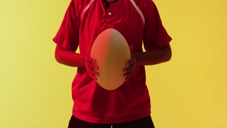 African-american-female-rugby-player-with-rugby-ball-over-neon-yellow-lighting