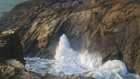 waves crashing and blowhole explodes in rocky coastal landscape, porth island, newquay, cornwall, united kingdom - wide shot