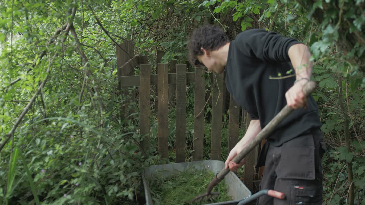 Young male gardener filling composter with garden cuttings using pitchfork
