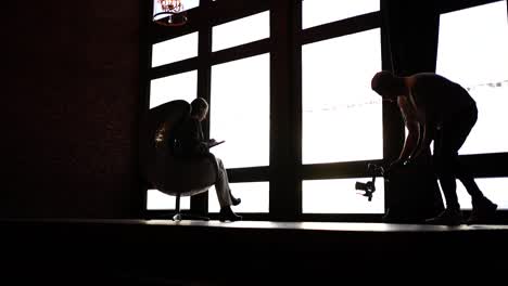 Silhouettes-of-female-model-sit-on-egg-chair-and-videographer-with-camera-gear