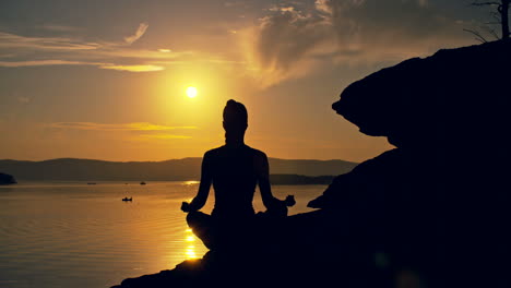 Hintergrundbeleuchtung-Einer-Frau,-Die-Yoga-Posen-Macht,-Die-Bei-Sonnenuntergang-Auf-Einem-Stein-Vor-Dem-Meer-Sitzen