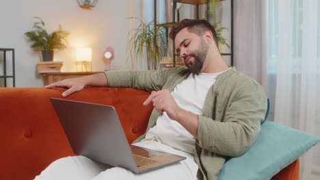 sleepy young man freelancer with brown hair cannot concentrate on work and types lazily on laptop