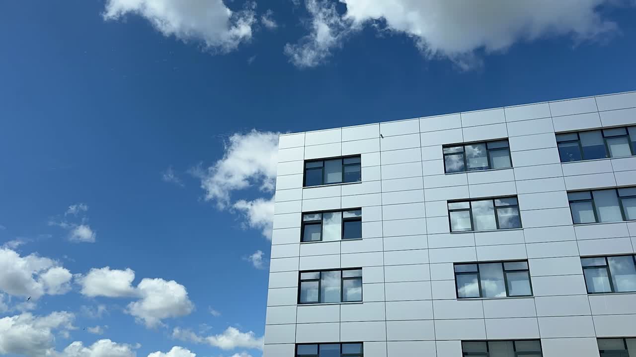 A timelapse of moving clouds over a corporate building, with a blue sky and modern cityscape in the background