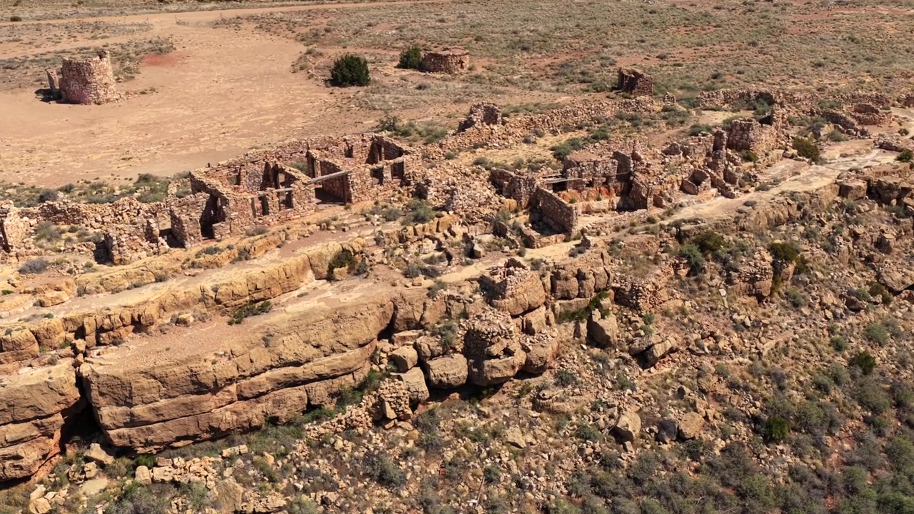 Engebeli bir uçuruma doğrudan inşa edilmiş, harap yığma duvarlardan oluşan geniş bir kompleksi sergileyen 4K UHD drone uçuşu. Çöl çalılıkları, güneşte kavrulan çatısız mimari kalıntıları çevreliyor