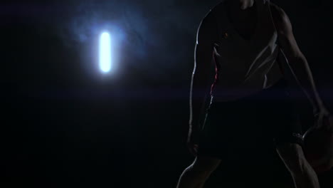 male urban basketball player dribbles ball in crouched position in an inner-city basketball court lit by single street light