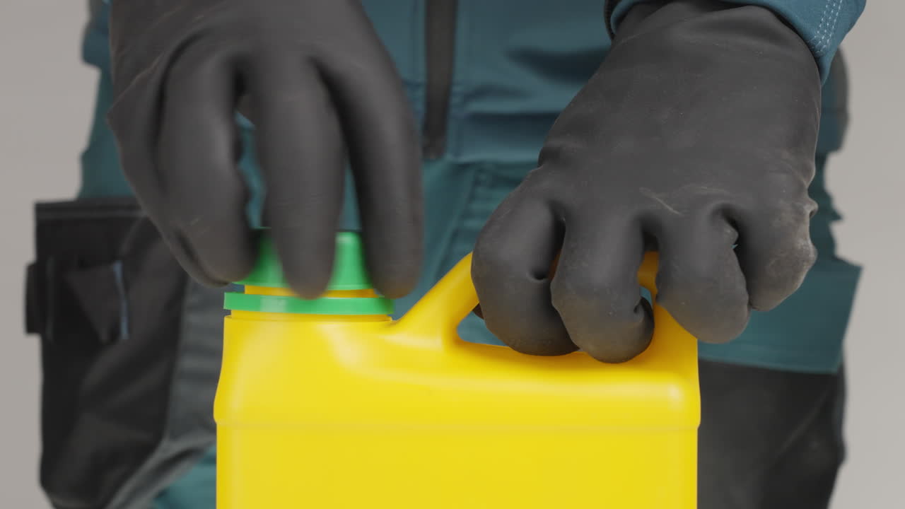 persona que abre un recipiente químico de plástico amarillo con guantes de protección