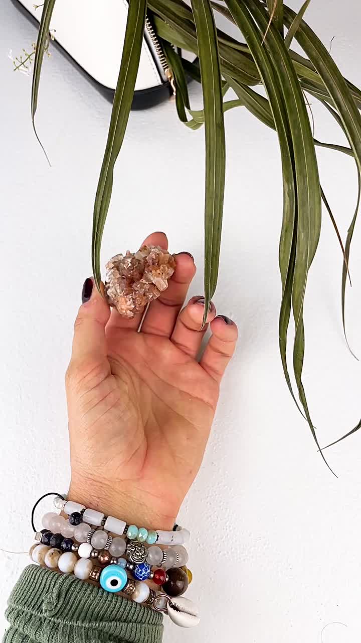 Woman holding a crystal with bracelets and a plant
