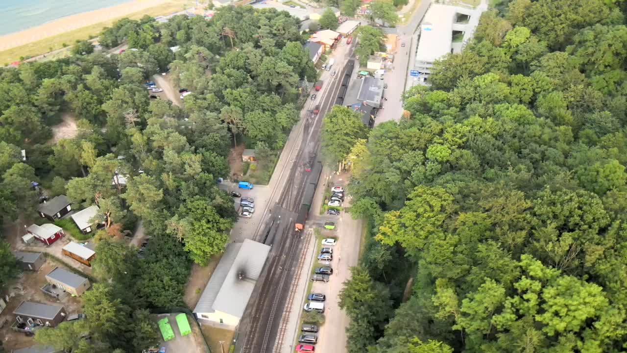 A vintage steam locomotive on Rügen powers through dense forest, surrounded by trees in a timeless natural setting, captured by drone.