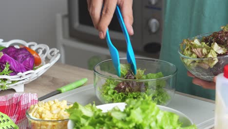 a man making salad, putting lettuces into a bowl for mixed salads