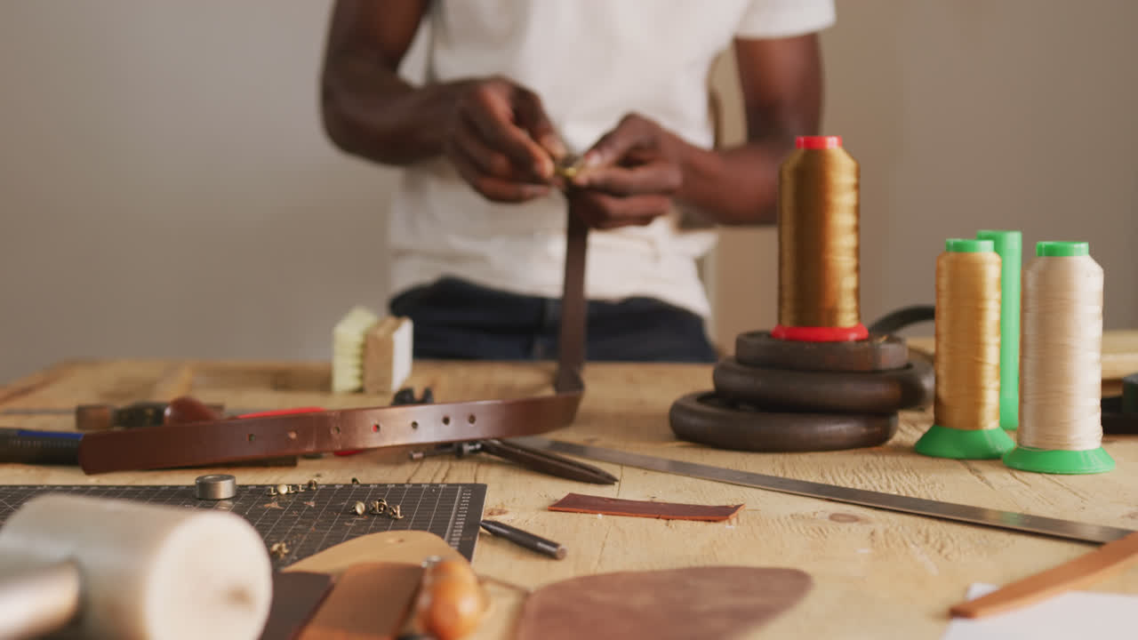 Hands of african american craftsman using tool to make a belt in leather workshop