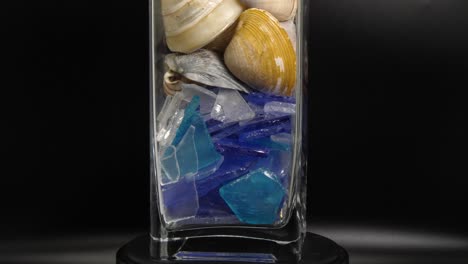 Close-up-view-of-a-rotating-glass-container-with-sea-shells,-still-shot