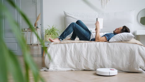man reading on bed with robot vacuum