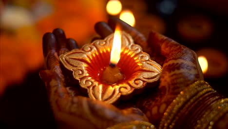 a female in traditional jewellery / bangles and heena tattoo holding diwali oil lamp / diya