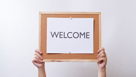 woman's hand shows the paper on board with the word welcome in white studio background with copy space