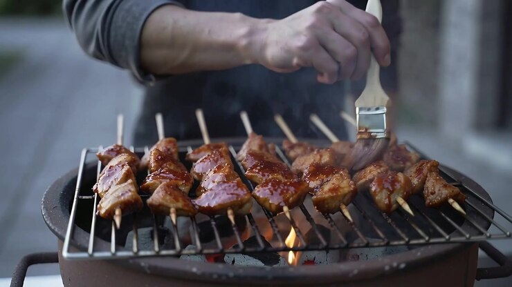Koki Mengoleskan Saus pada Tusuk Sate di Atas Panggangan Arang