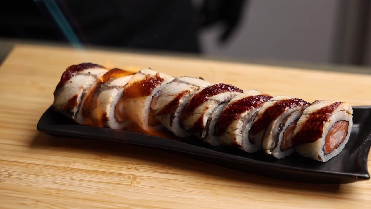 Primo piano di uno chef che scotta rotoli di sushi con una torcia da cucina