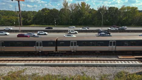 Epic-aerial-view-of-passenger-trains-crossing-parallel-to-highway,-Atlanta-city-road-traffic,-GA,-USA